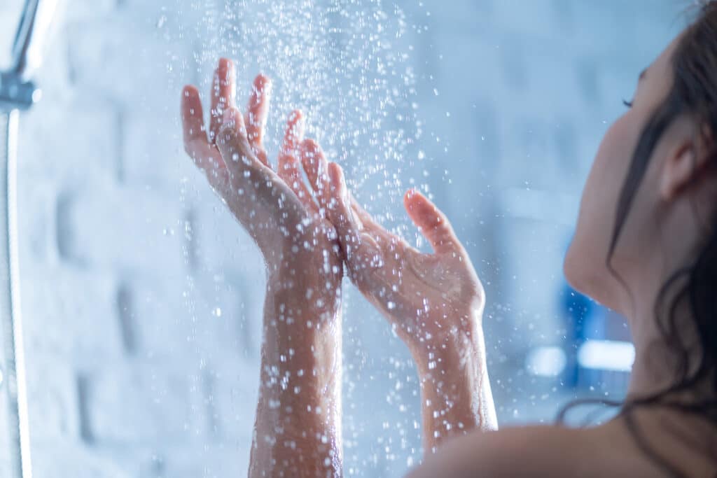 Personne sous la douche, mains levées recevant des milliers de gouttes d'eau scintillantes, instant de fraîcheur.