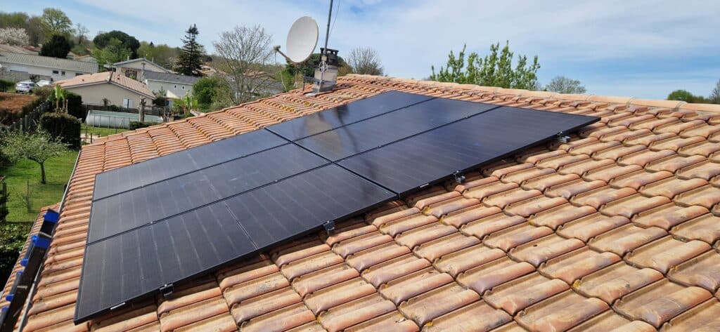 Installation de 6 panneaux solaires noirs sur un toit en tuiles terre cuite et des maisons en arrière-plan.
