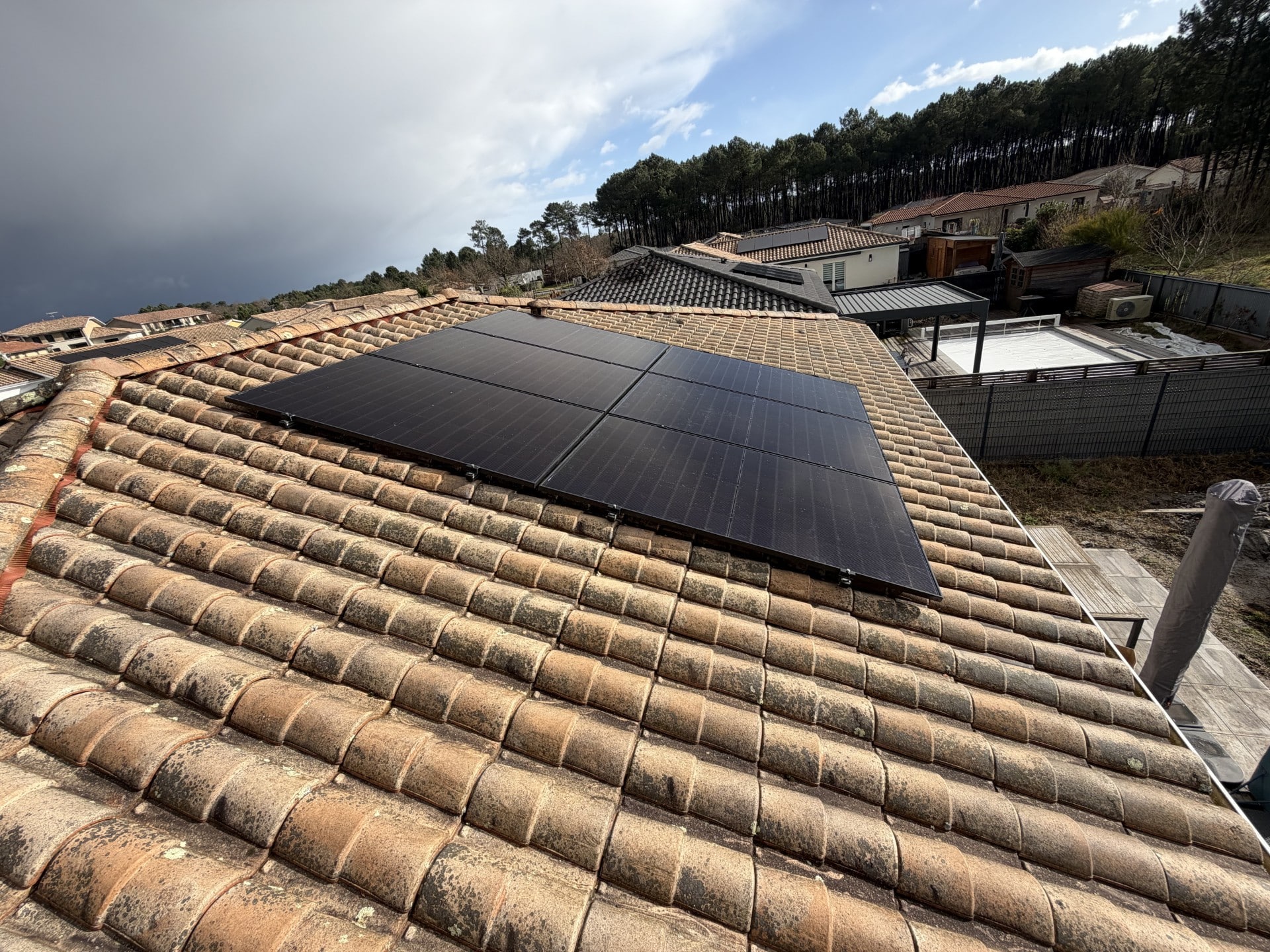 Installation de panneaux solaires sur une toiture en tuiles Six panneaux solaires noirs sur une toiture en tuiles romanes dans un quartier résidentiel arboré.